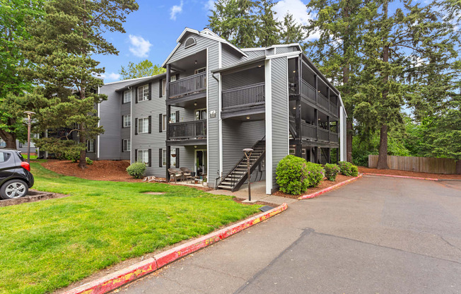 A grey apartment building with a car parked in front.
