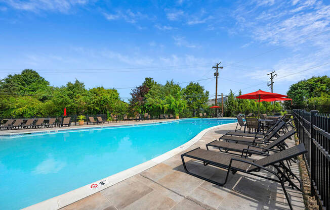 A pool with a red umbrella and lounge chairs.