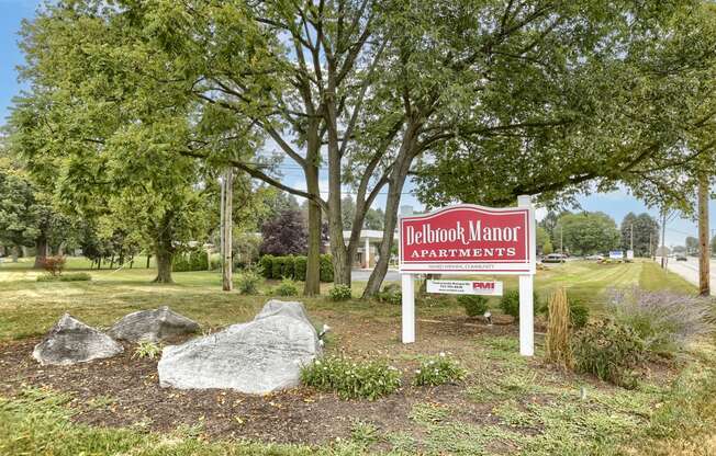 Mechanicsburg Apartments | Delbrook Manor Apartments | a sign in front of a grassy area with trees in the background