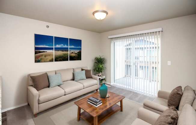 A living room with a couch, a coffee table, and a large window with a view of the outside.