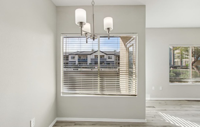 A room with a large window covered by white blinds and a chandelier hanging from the ceiling.