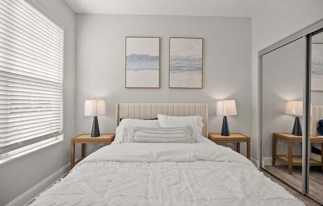 A bedroom with a large bed, two lamps, and two framed pictures on the wall.