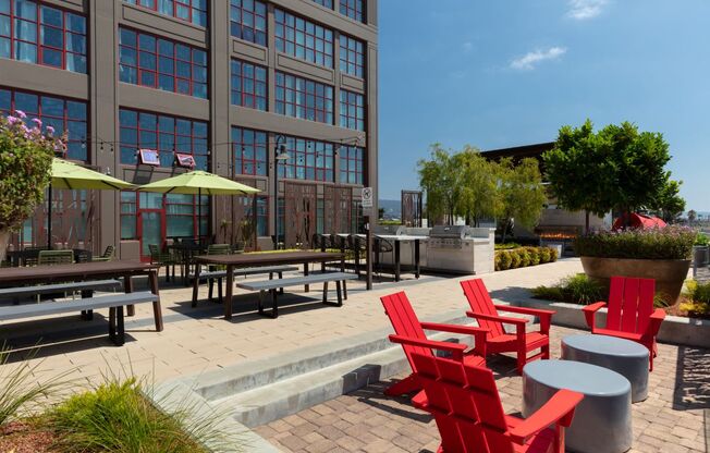 a patio with red chairs and umbrellas in front of a building