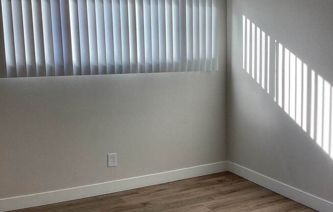 A room with wooden flooring and a window with blinds.