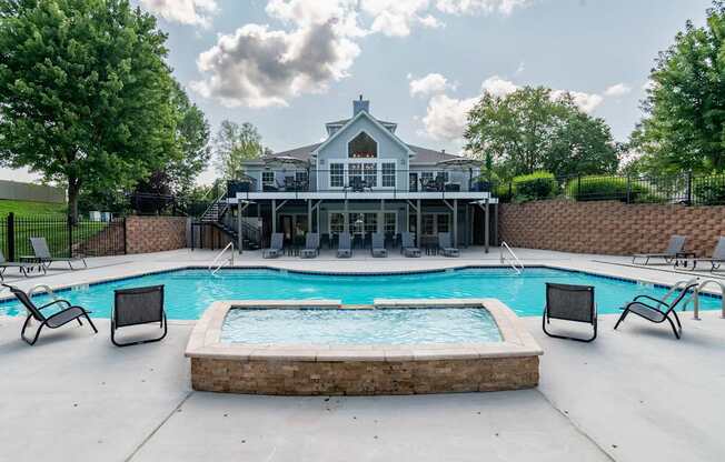 A pool with a hot tub and a house in the background.