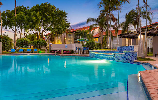 A swimming pool surrounded by palm trees and a building in the background.