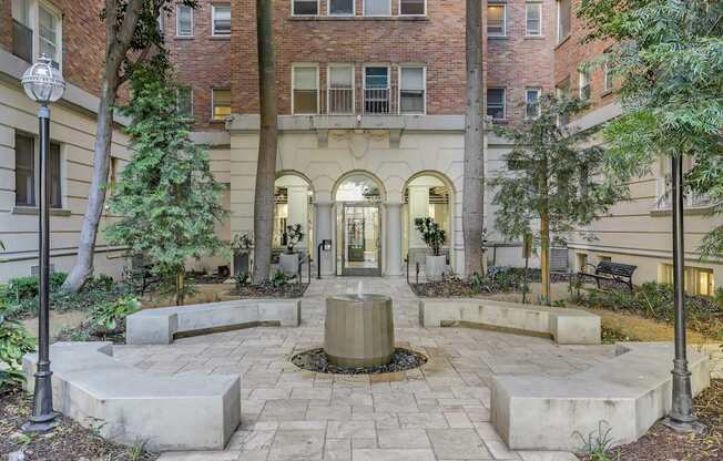 A courtyard with a fountain surrounded by trees and benches.