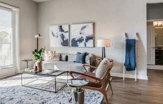 A modern living room with a glass coffee table and a large abstract painting on the wall.