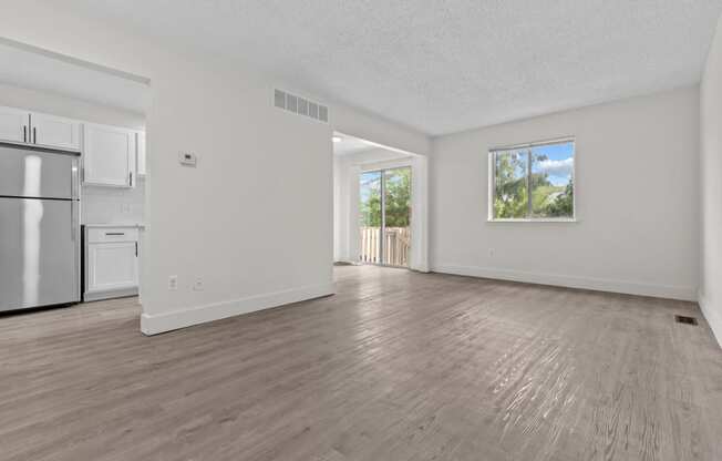 the living room and kitchen of an apartment with white walls and wood floors