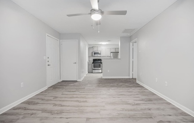 an empty living room with a ceiling fan and a kitchen