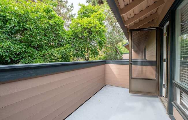 A balcony with a sliding door and a view of green trees.
