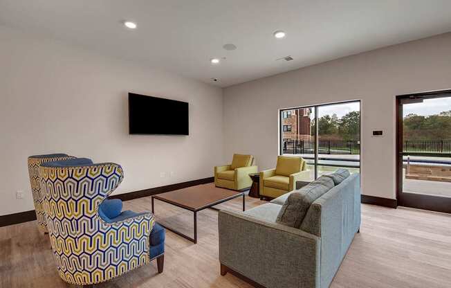 A modern lounge here at The Park featuring a gray sofa, blue patterned accent chairs, yellow armchairs, and a coffee table, with large windows bringing in natural light and creating a welcoming space.