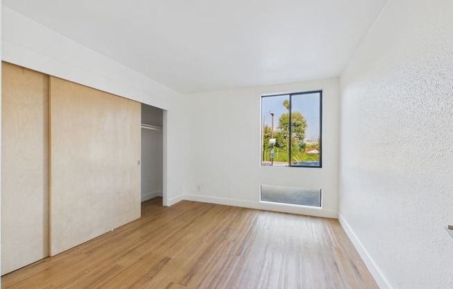 A room with wooden floors and a window showing a view of trees.