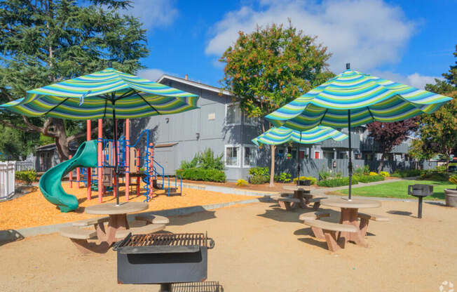 A playground with a green slide and two blue and white striped umbrellas.