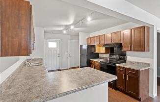 A kitchen with track lighting, wood cabinets, and black appliances at Muskego School Apartments