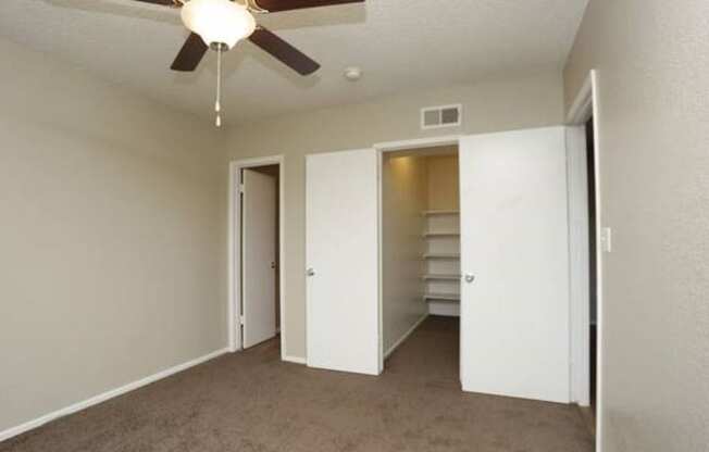 an empty living room with a ceiling fan and a closet