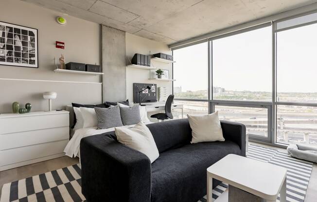 a living room with a black couch and a large windowat One Foundry Way, St. Louis, 63110