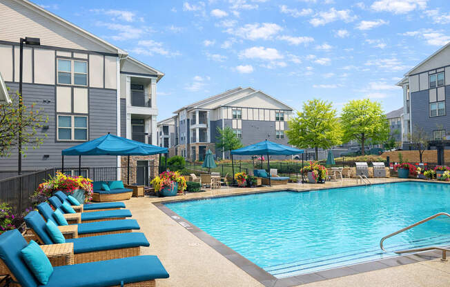 A swimming pool surrounded by lounge chairs and umbrellas in a residential area.