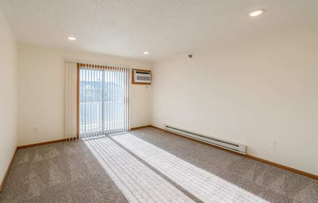 the living room of an apartment with carpet and a sliding glass door. Fargo, ND Eagle Run Apartments