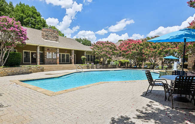 A pool surrounded by chairs and a house with a stone wall.