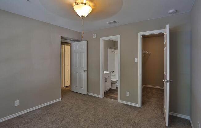 carpeted bedroom with open bathroom and closet doors