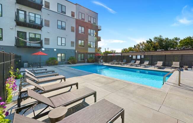 a swimming pool with lounge chairs and umbrellas in front of an apartment building