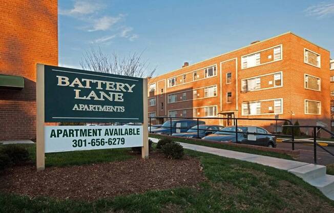 A sign for Battery Lane Apartments is in front of a brick building.