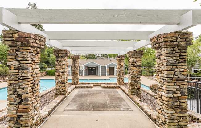 A white pergola with stone pillars leads to a pool area.