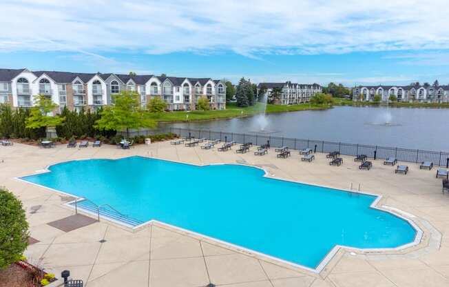 a large swimming pool with chaise lounge chairs next to a lake with apartment buildings in the