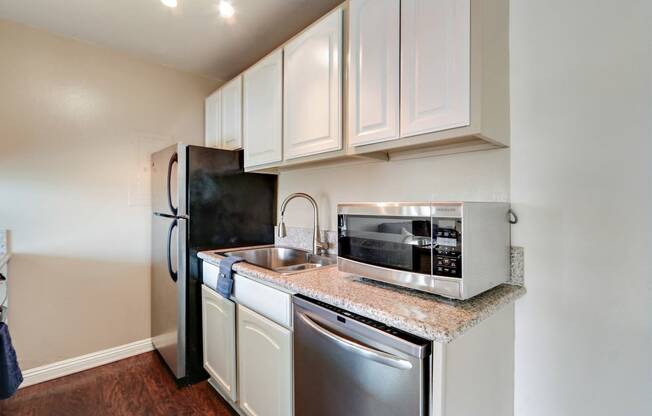 Kitchen with stainless steel 2 door refrigerator, double kitchen sink, microwave, dishwasher, granite countertops, white kitchen cabinets