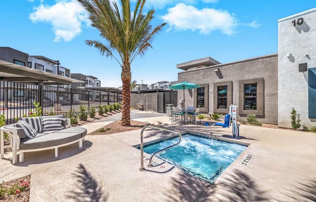 Modern apartment complex with a luxurious outdoor patio, featuring a cozy seating area, vibrant palm tree, and inviting jacuzzi under a clear blue sky at Summit on Boulder Apartments, just 20-minutes from Las Vegas.