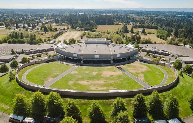 A large stadium with a grassy field in the center and cars parked around it.
