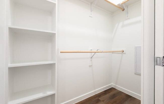 a walk in closet with white shelves and a wood floor
