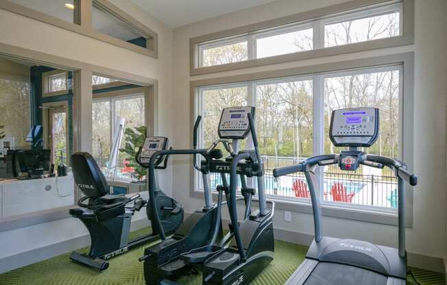 Gym at the Retreat at Indian Lake apartments in hendersonville with three different cardio machines facing out a large window.