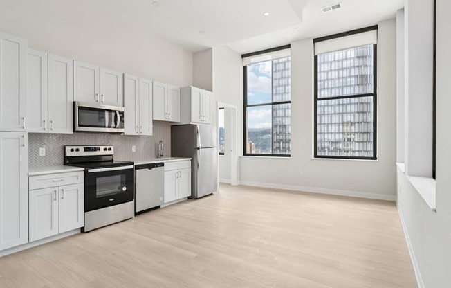 A kitchen with white cabinets and appliances, a wooden floor, and a view of the city through the windows.