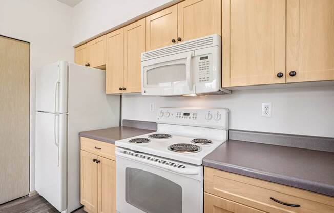 A kitchen with a white refrigerator, microwave, stovetop oven, and wooden cabinets at The Madison Apartments in Olympia, WA