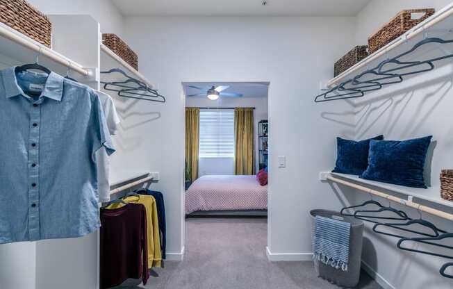 a walk in closet with a bedroom in the background and shelves with clothes on them