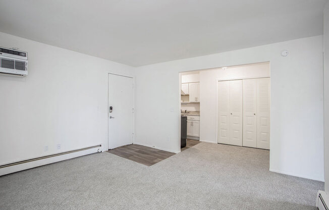 an empty living room with a kitchen in the background