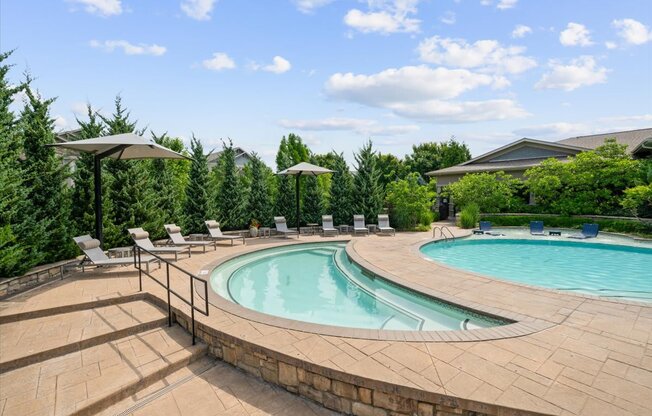 A large outdoor swimming pool surrounded by a stone wall and lounge chairs.