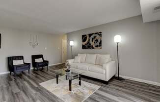 A living room with a white couch, a black chair, and a glass coffee table.