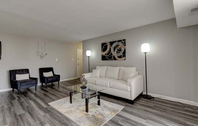 A living room with a white couch, a black chair, and a glass coffee table.