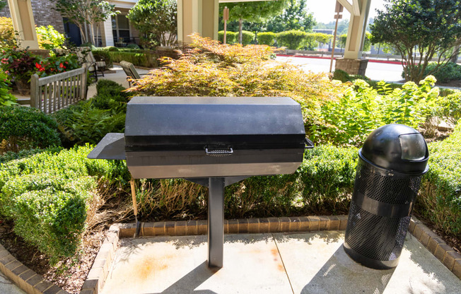 a charcoal grill and a trash can sit in front of a garden