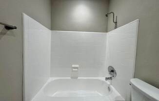 A white bathroom with a white tub and a white shower head.