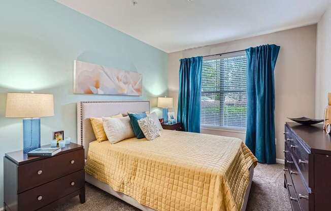 A bedroom with a bed, nightstand, and window with blue curtains.