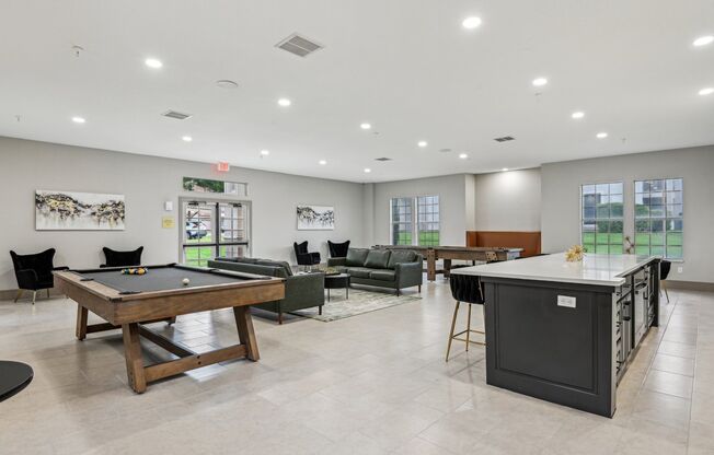 A billiard table is in the middle of a room with a pool table, a couch, and a bar.