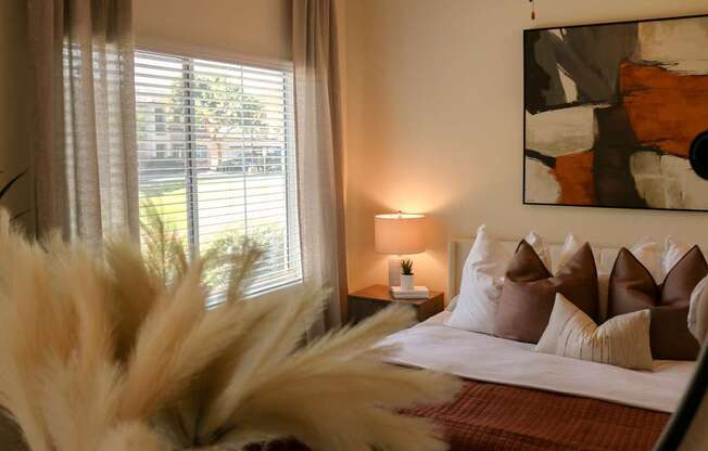 A bedroom with a bed, pillows, a lamp, and a painting on the wall.