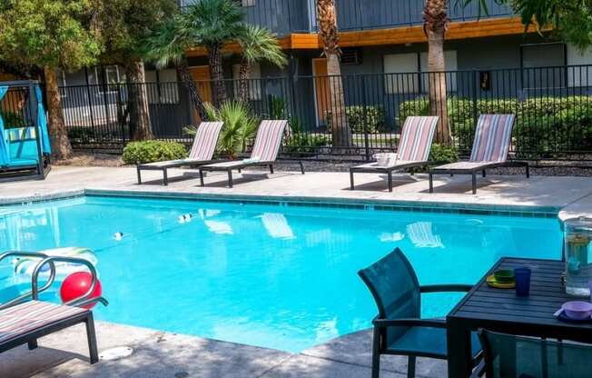 Fifteen 50 apartments near Las Vegas strip Community pool surrounded by tall gated fence, greenery, and patio loungers.