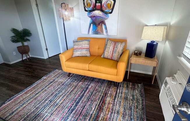 A living room with a yellow couch and a colorful rug.
