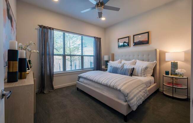 A bedroom with a large bed, a ceiling fan, and a window with curtains.