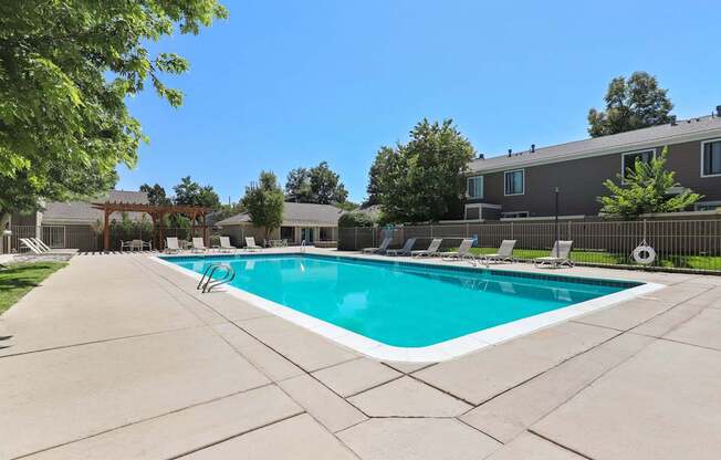 A large swimming pool surrounded by a concrete patio and lounge chairs.